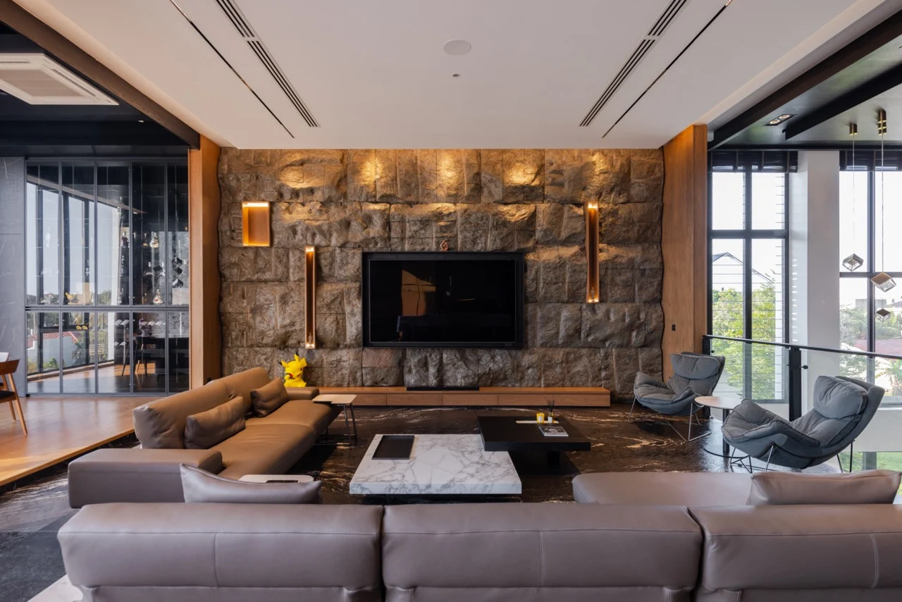 Main living room at Muar Residence, with a stone feature wall, flush ceiling speakers and linear air conditioning diffusers.